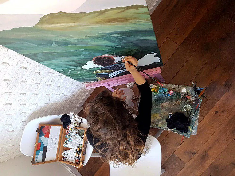 Kate seen from above, painting a large mountain canvas on a pink easel
