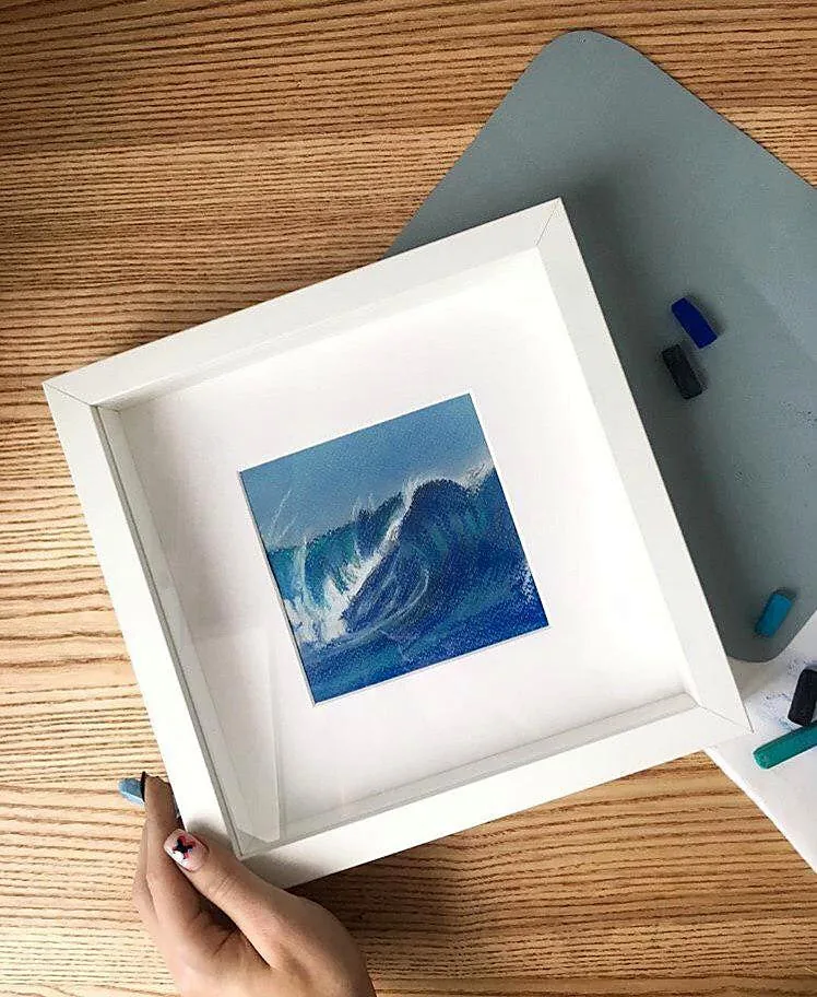 Hand holding the framed Surfing Wave pastel next to pastel sticks