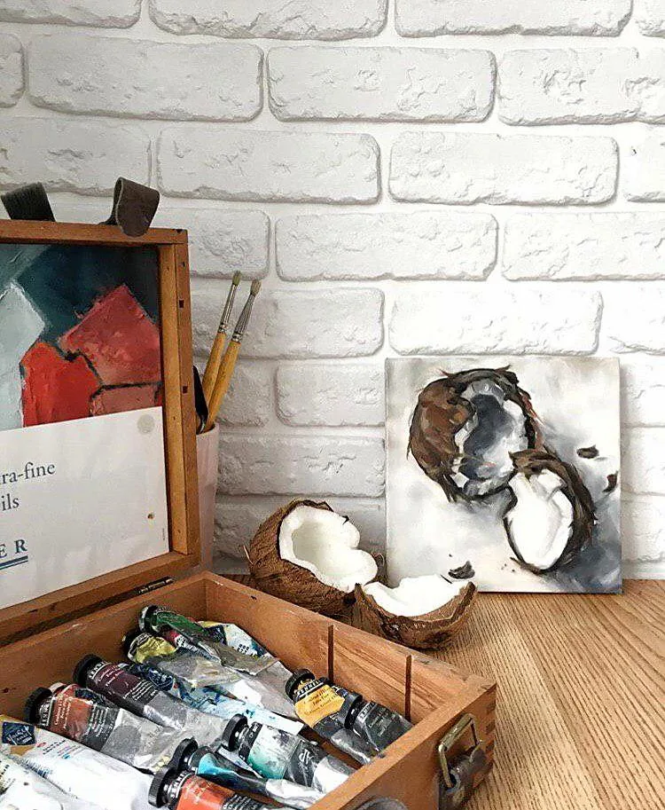Cracked Coconut painting beside real coconut halves and a box of oil paints